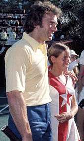 man stands next to a girl as they both face to the left, smiling.